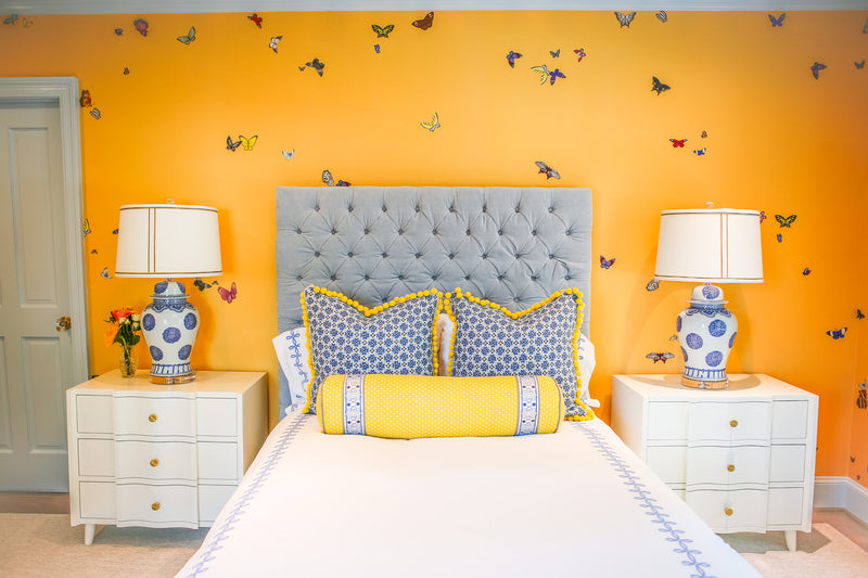 Head-on view of yellow bedroom with butterfly wallpaper. Blue headboard, blue, white, and yellow linens