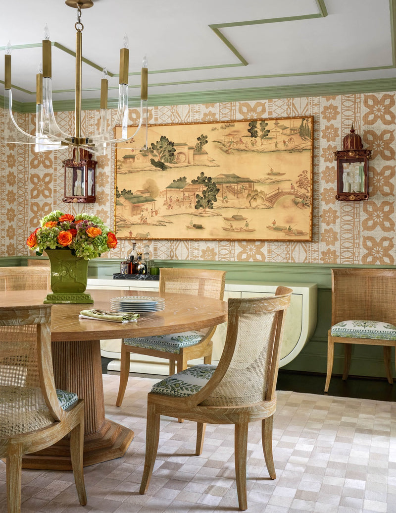 Dining area with round table, woven chairs, and printed wallcovering.