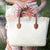 Picture of woman holding straw beach tote with brown leather handles