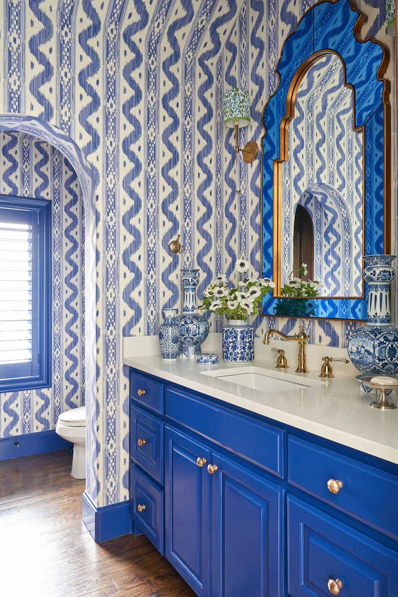 Bathroom sink area with blue cabinets and blue and white patterned wallcovering