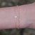 Thin gold bracelet with a diamond flower on a person's arm