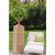 Outdoors on grass, a chair and ottoman sit to the right of a rattan urn and pedestal with a fern in the urn